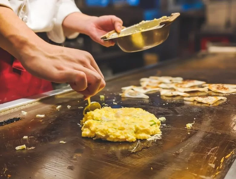 Japanese chef cooking okonomiyaki on a flat top grill